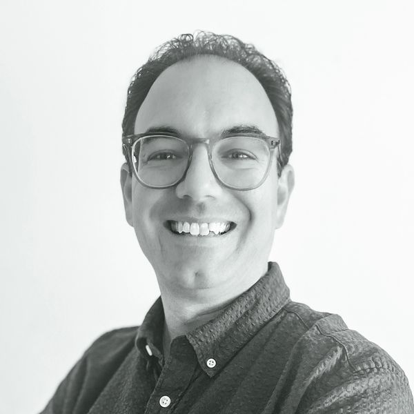 Black-and-white portrait photograph of Nicholas Jay. He is smiling at the camera and wears glasses.