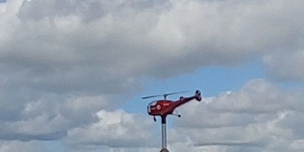 A red helicopter weather vane against a cloudy sky.