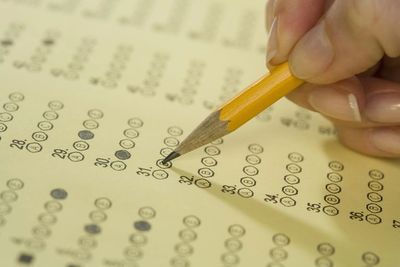 Hand filling out a multiple-choice answer sheet with a pencil.