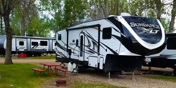 Sundance XLT RV parked in a green, tree-filled campground with picnic table.