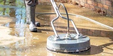 Man cleaning concrete patio with a surface cleaner near a brick wall.