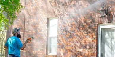 Man power washing the exterior brick wall of a house on a sunny day.