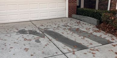 A driveway with scattered dry leaves and dark stains in front of a garage door.