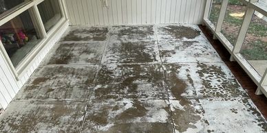A worn concrete floor on a screened porch with white wooden walls and a brick threshold.