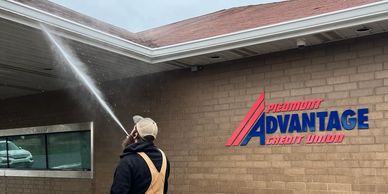 Worker power washing the exterior wall of Piedmont Advantage Credit Union.