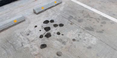 Oil stains scattered on a concrete parking lot surface near wheel stops.