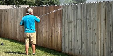 Man power washing a wooden fence on a sunny day.