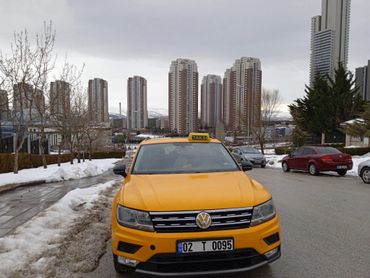 Yellow Volkswagen taxi parked on a snowy city street with tall buildings.