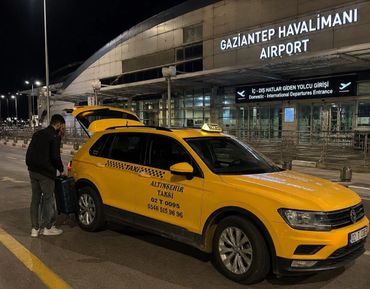 A yellow taxi at Gaziantep Airport with a passenger loading luggage.