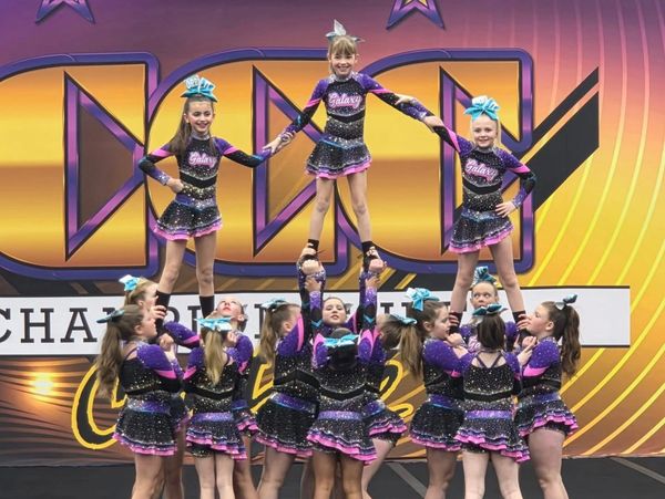 Cheerleading team performing a pyramid stunt in sparkling purple and pink uniforms.