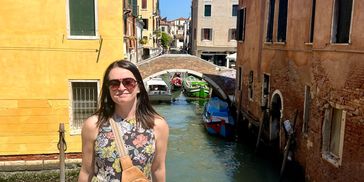 Woman in floral dress standing by a canal with colorful buildings in Venice.