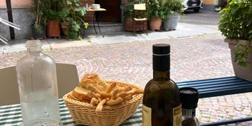 Outdoor café table with bread, olive oil, and sunglasses on a checkered tablecloth.