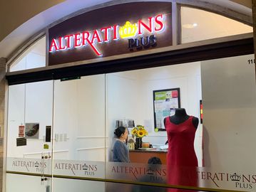 Exterior of a tailoring shop named Alterations Plus with a red dress on a mannequin.