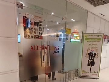 Glass entrance of Alterations Plus shop with service banner and floor reflection.