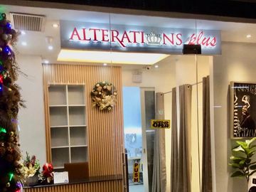 Entrance of a modern tailoring shop named Alterations Plus, decorated for Christmas.