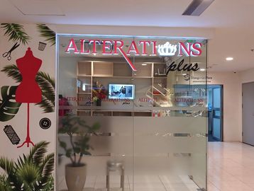 Entrance of a tailor shop named Alterations Plus with sewing-themed wall art.