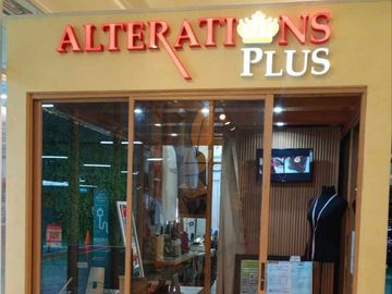 A tailor shop named Alterations Plus with glass doors and a mannequin inside.