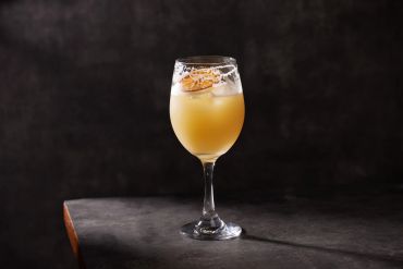 A cocktail with an orange twist in a wine glass.