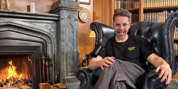 Man sitting in a leather armchair by a fireplace in a cozy library setting.