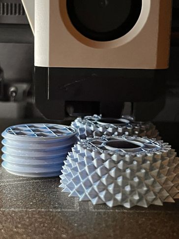 Close-up of 3D printed parts with intricate designs under a 3D printer nozzle.