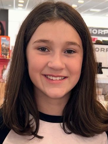 Smiling young girl with shoulder-length brown hair in a store.
