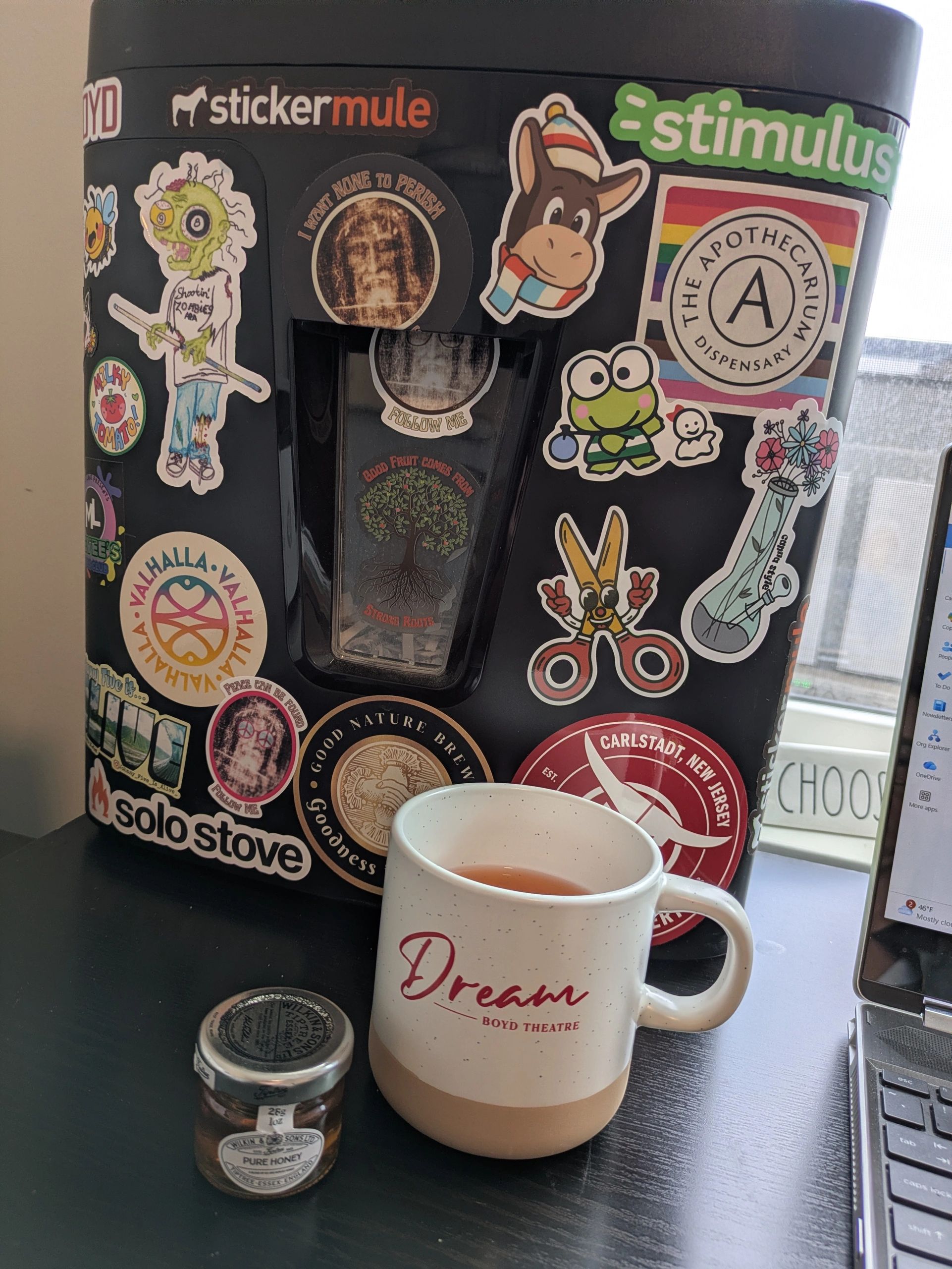 A black stove covered in colorful stickers with a white mug and a honey jar on a desk.