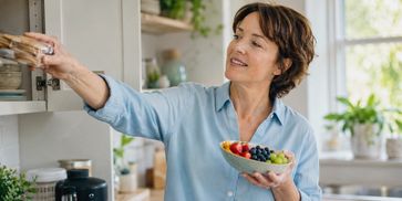 A woman putting biscuits away while choosing fruit, representing healthier habits.