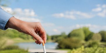 A hand discarding an unlit cigarette outdoors, representing freedom from smoking.