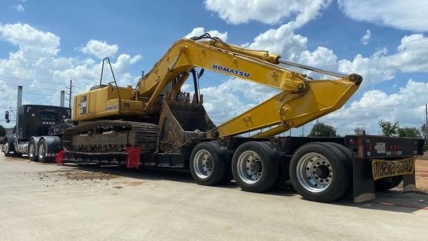 Yellow Komatsu excavator loaded on a flatbed trailer under a blue sky.