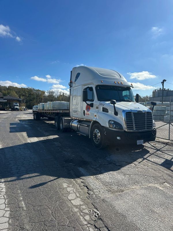 White semi-truck with flatbed trailer loaded with goods parked outdoors.