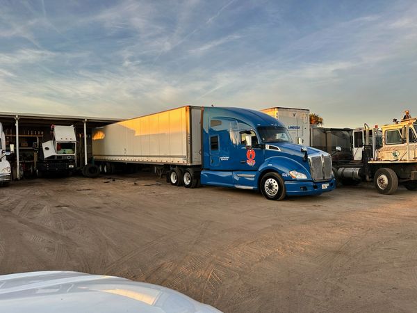 Blue semi-truck parked in a lot with other trucks during sunset.