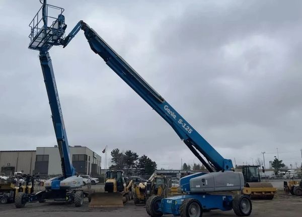 Two blue Genie S-125 boom lifts extended towards each other under a cloudy sky.