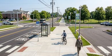 A sunny day scene with a cyclist and a pedestrian on a wide sidewalk near a bus stop.