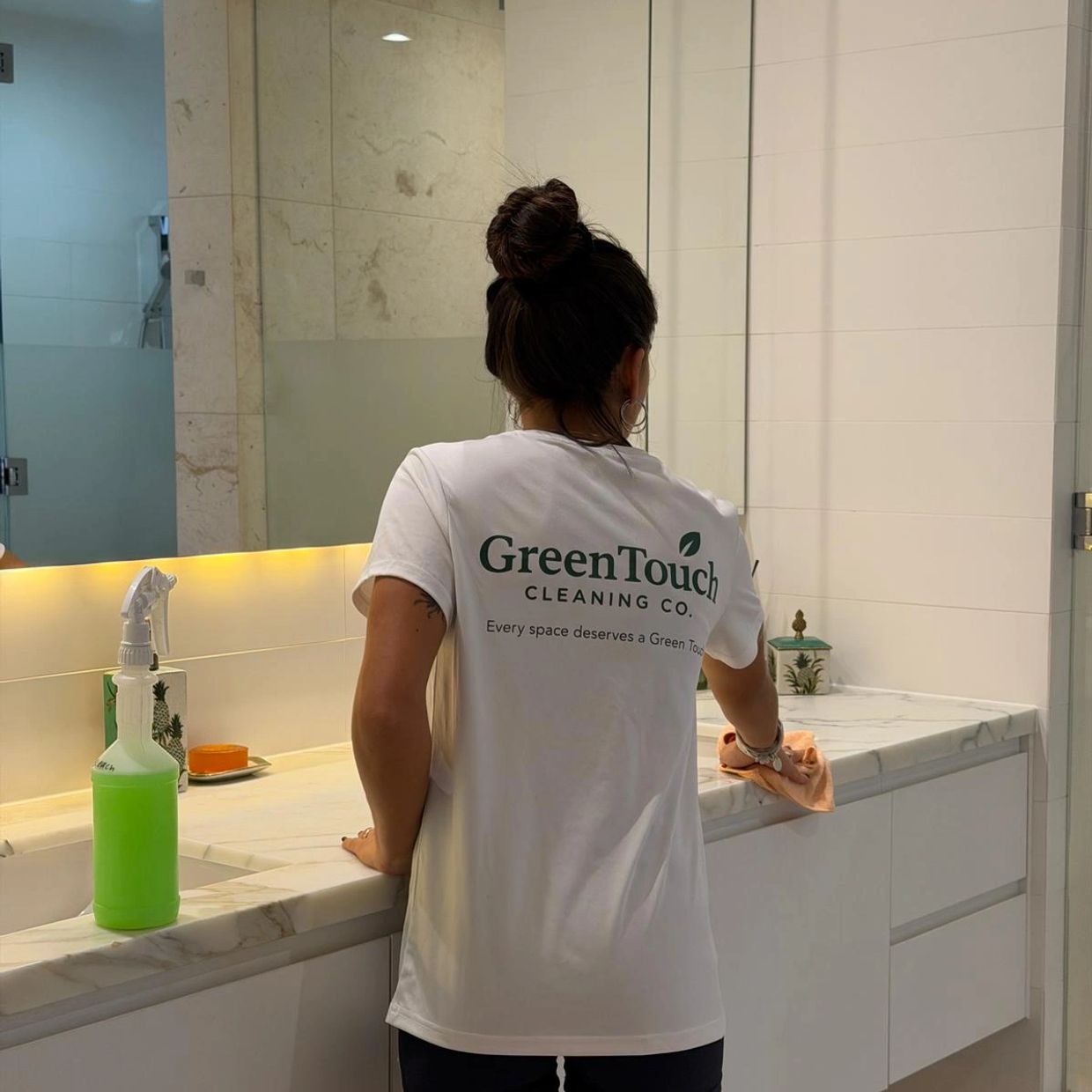 Woman cleaning a bathroom counter wearing a GreenTouch Cleaning Co. shirt.