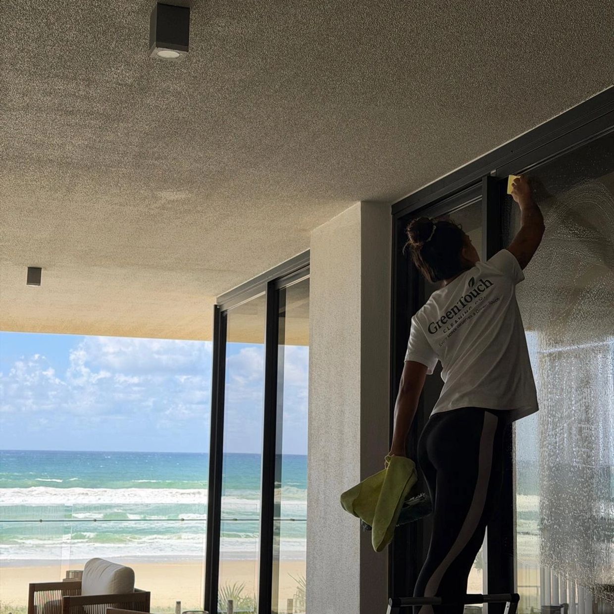 Person cleaning large glass windows with ocean view in the background.