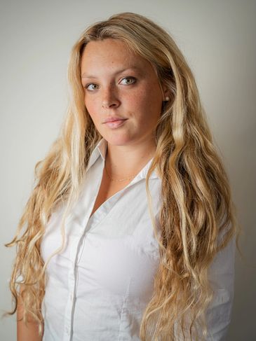 Blonde woman with long wavy hair wearing a white shirt.