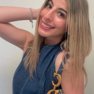 Smiling woman with blonde hair wearing a denim top and holding a bag.