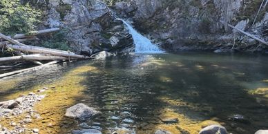 Small waterfall flowing into a clear pool surrounded by rocky terrain.