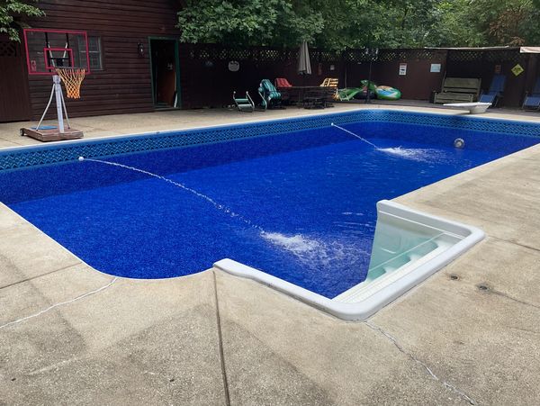 A clean backyard pool with water jets and a basketball hoop.