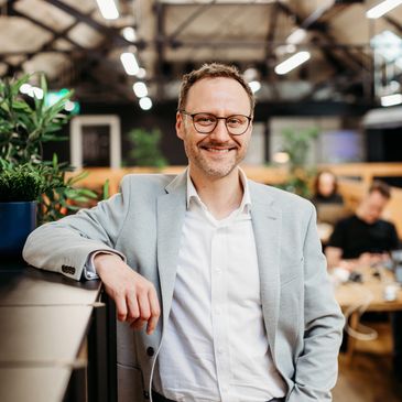 Smiling man in glasses and blazer in a modern office environment.