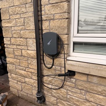 Electric vehicle charging station mounted on a stone wall with cables.