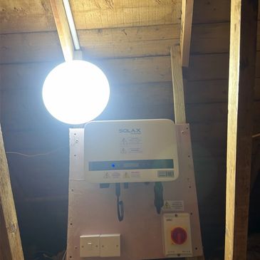 A bright ceiling light and a mounted solar inverter in an attic.