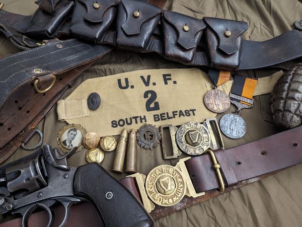 Vintage UVF South Belfast armband with an Irish Volunteer buckle along with medals, bullets, and a revolver.