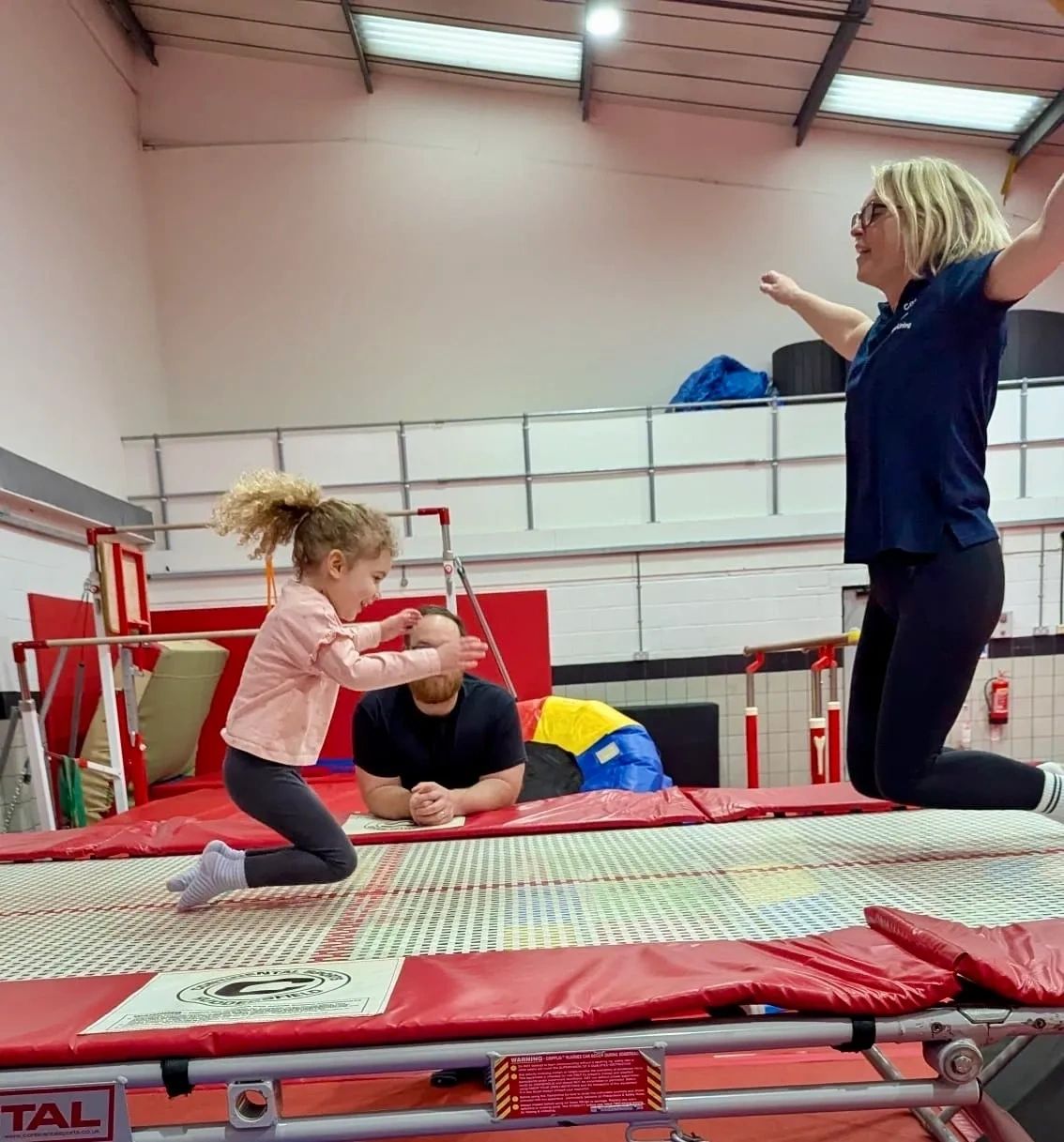 A child and an adult joyfully jumping on a trampoline indoors.