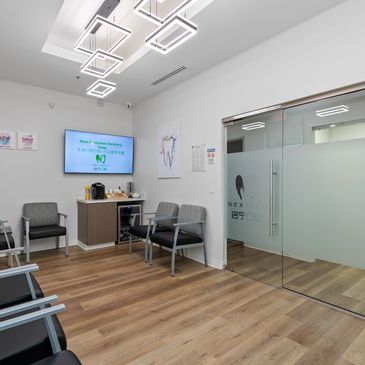 Modern dental office waiting room with gray chairs and wood flooring.