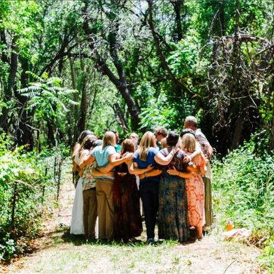 A group embraces in a sunny forest clearing, symbolizing unity.