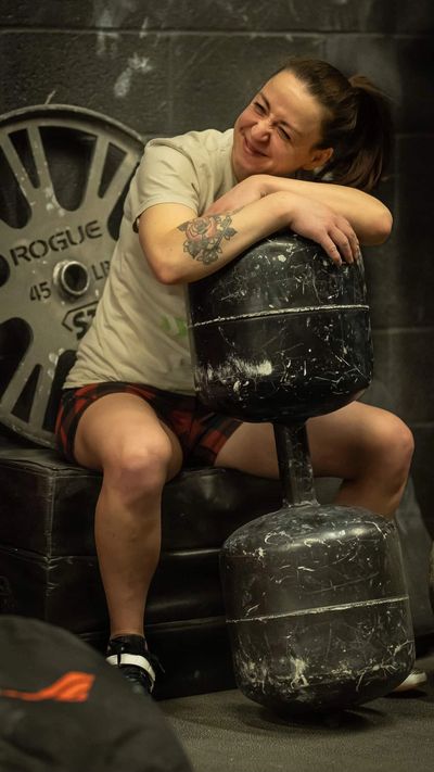 Women sitting holding a giant Dumbbell smiling