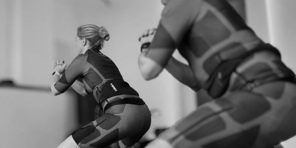 Two people in black and red workout suits doing squats indoors.