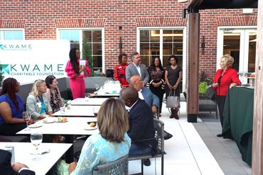 A woman in red speaks to an audience on a patio.