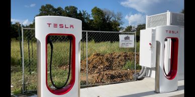Tesla electric vehicle charging stations outdoors beside a fenced area.